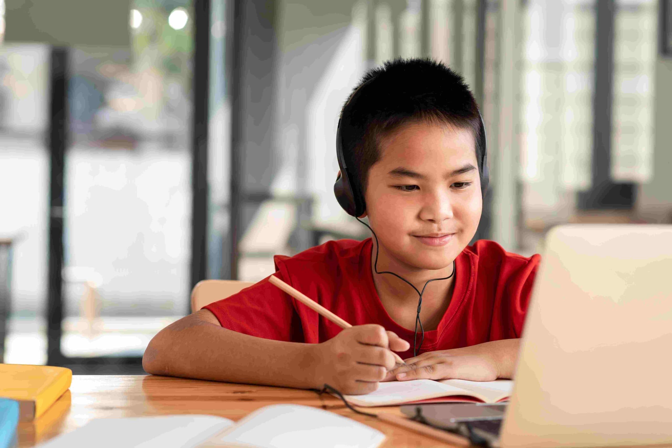 A Year 3 boy wearing headphones works through maths practice beside his laptop