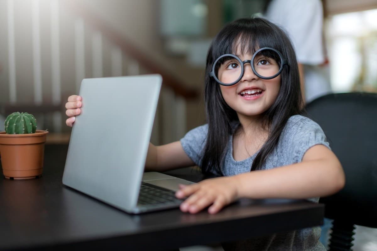 A cheerful young girl in round glasses at her laptop during an online English lesson