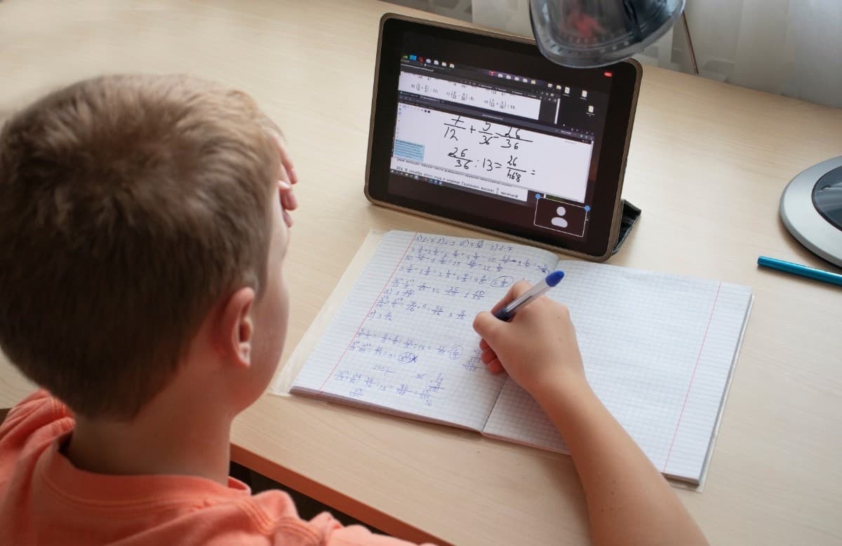 A Year 5 student solving fraction problems in his notebook while following a tablet maths lesson