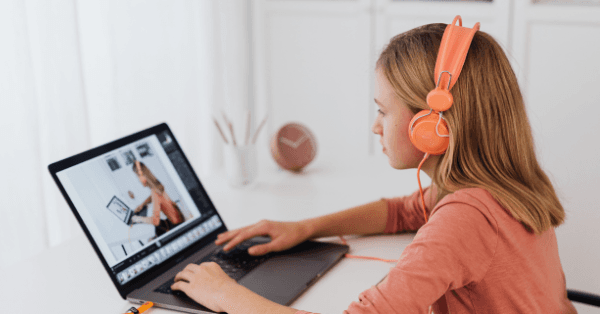 A girl in orange headphones following a live online lesson on her laptop