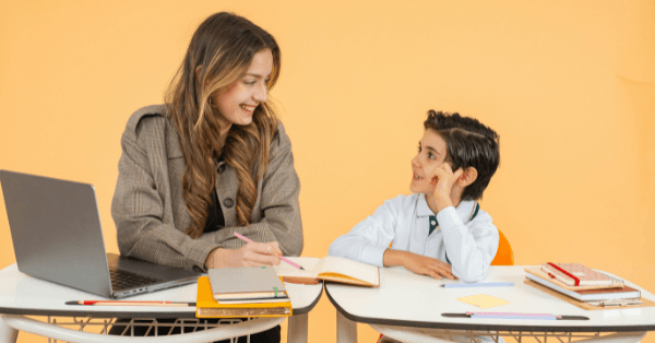 A tutor and a young student in school uniform smiling at each other during a lesson