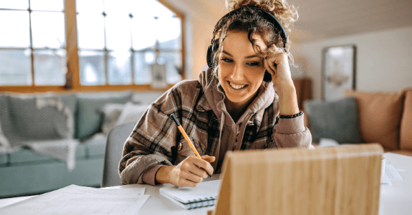 A student smiling while writing notes beside her tablet at home