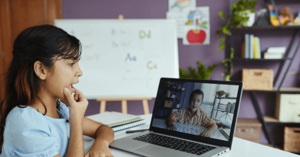 A young girl answering her classmate on screen during an online lesson at home