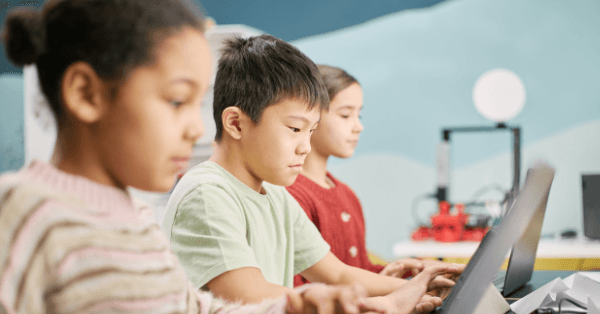 Three children concentrating on laptops in a technology classroom