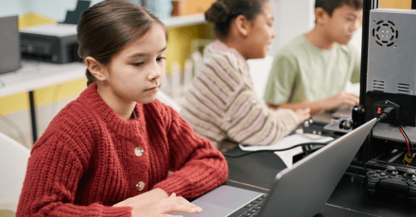 A girl in a red jumper working on a laptop in class alongside her classmates