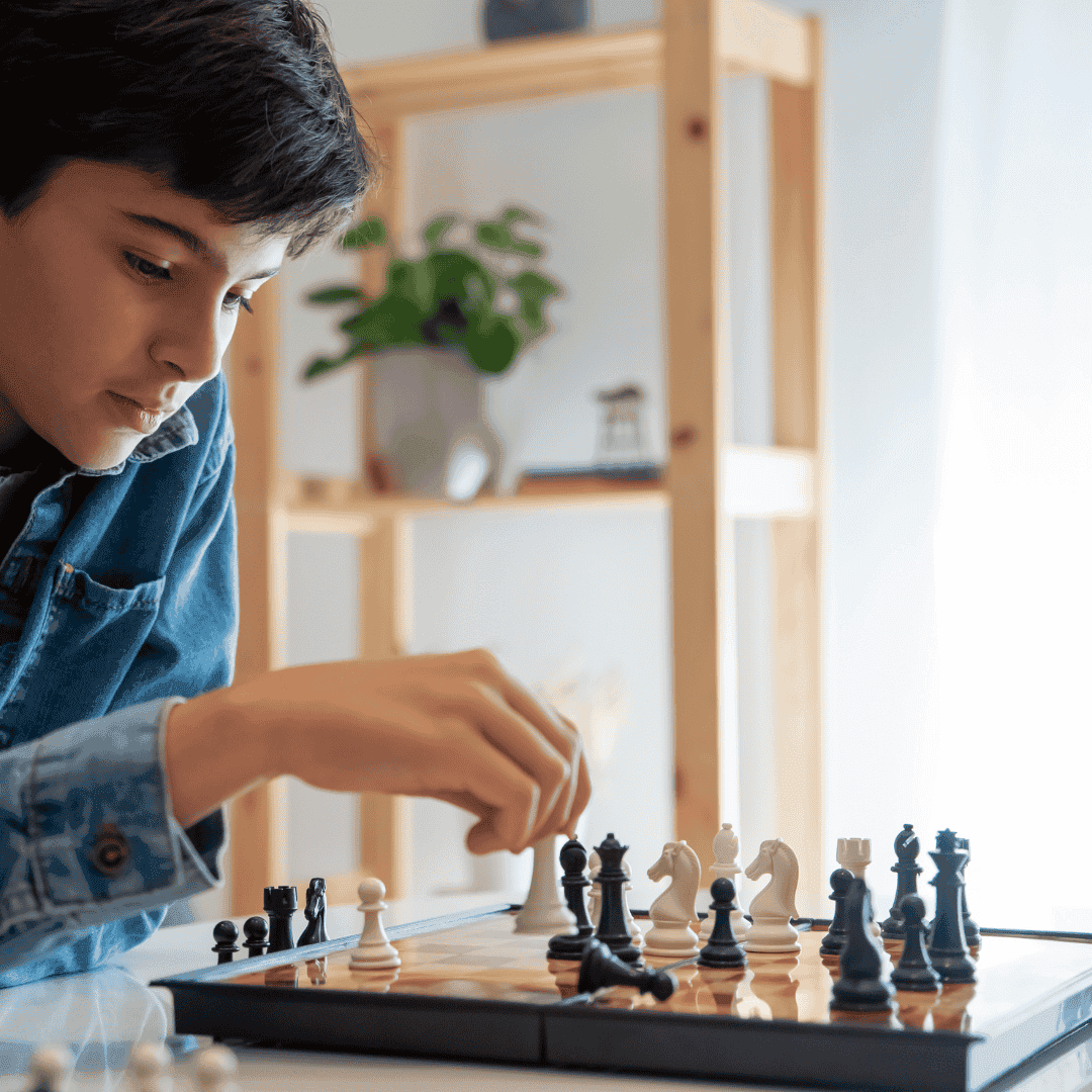 A young student concentrating as he makes his move on a chessboard at home