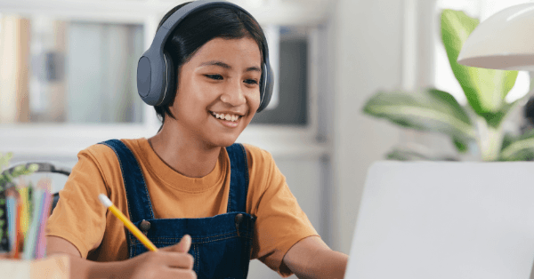 A smiling student in headphones taking notes during an online class
