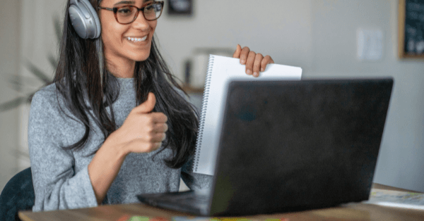 An online tutor holding up a notepad and giving a thumbs up during a video lesson